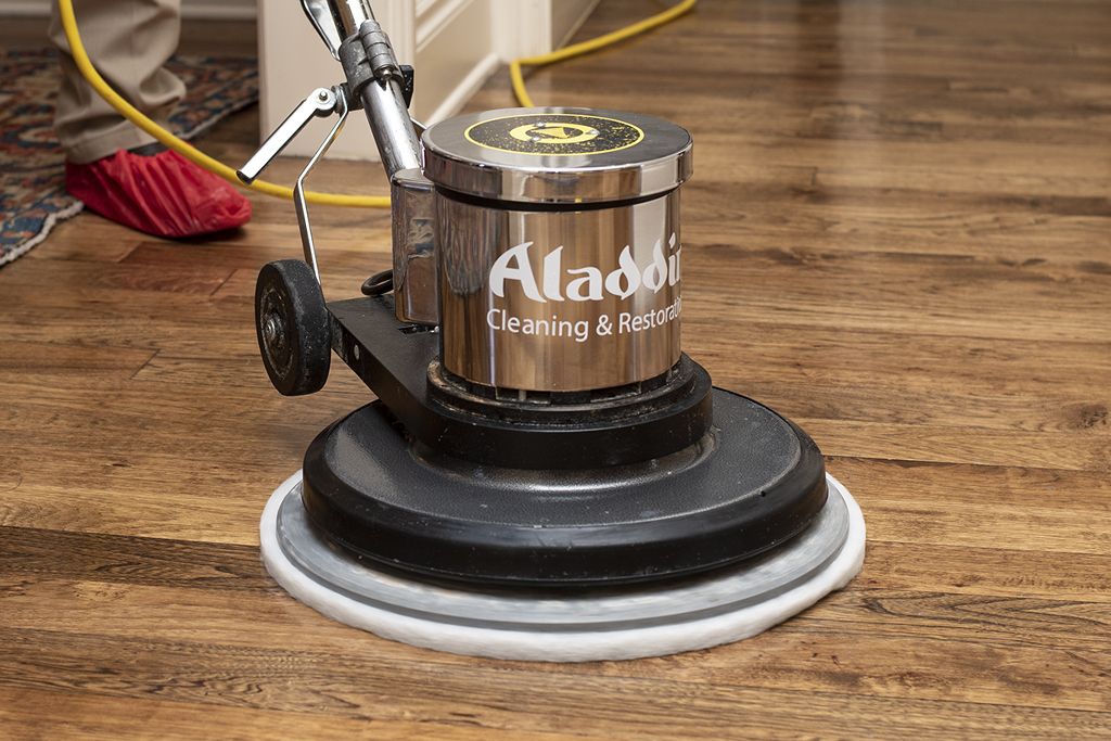 An Aladdin employee cleaning a wooden floor with tool.