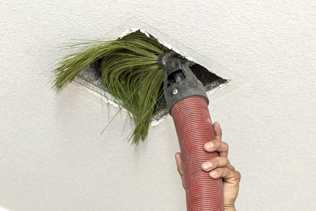 An Aladdin employee cleaning an air duct with tool.