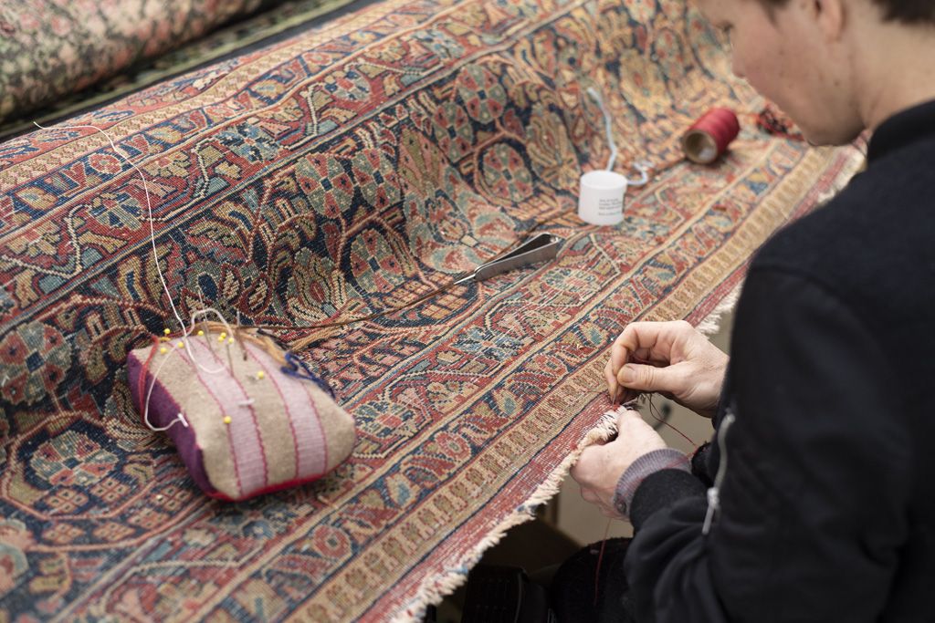 Aladdin Employee repairing stitching on a rug.