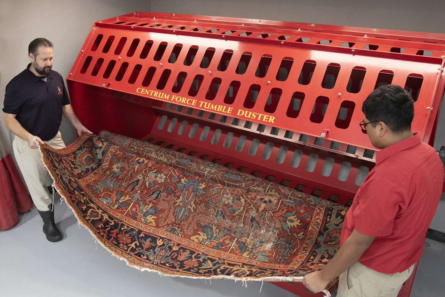 An oriental rug is inserted into a Centrum Force Tumble Duster to remove dry soil prior to wet cleaning process